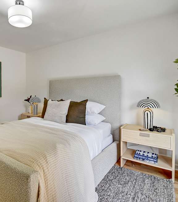 A bedroom with a bed, nightstand, and a painting on the wall.