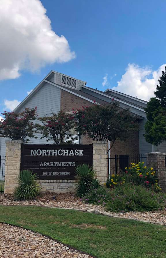 The image shows the front of Northchase Apartments with a sign and two decorative flags.