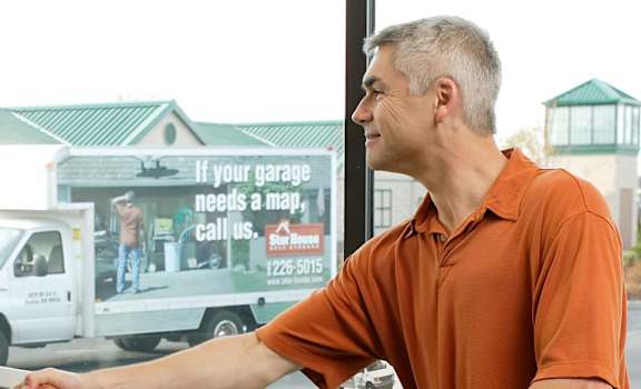 A man in a black shirt is handing over a white box to a man in an orange shirt.