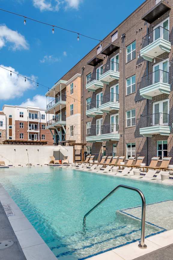 an outdoor swimming pool with lounge chairs in front of an apartment building