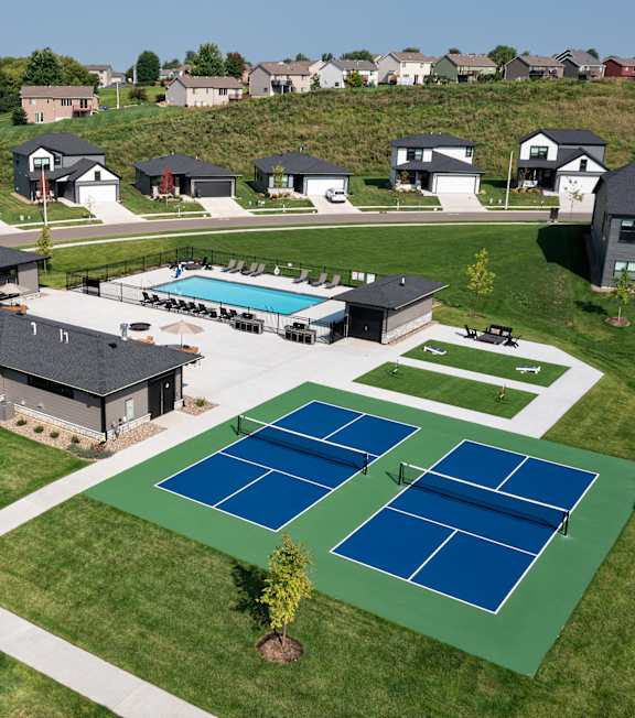 A tennis court is located in the foreground of a residential area.