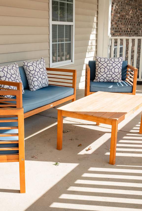 A wooden bench with cushions sits on a patio.