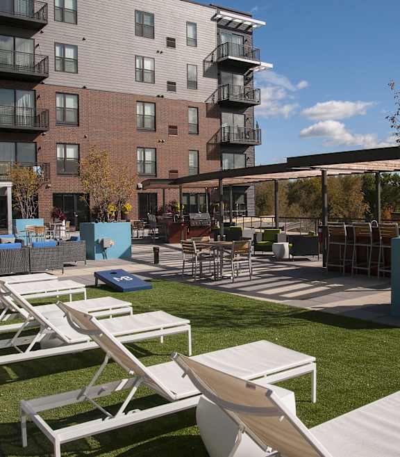 an outdoor lounge area with white lounge chairs and tables in front of an apartment building