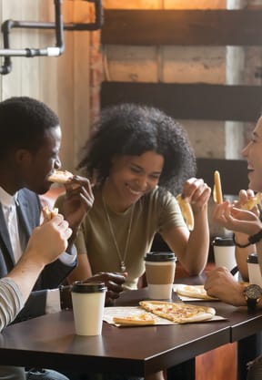 people sitting around a table eating pizza and drinking coffee