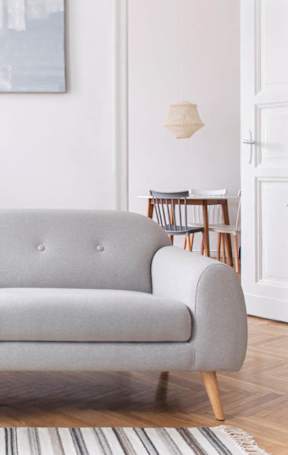 A grey couch with a white throw blanket on it.