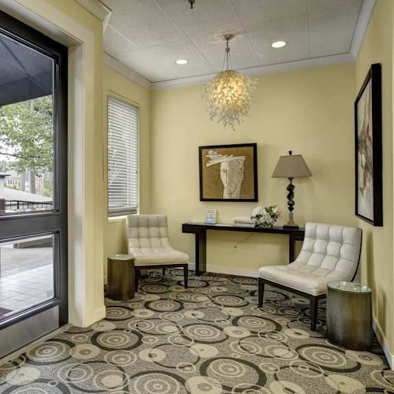 A corner with two white plush chairs, artwork, and a lamp for the residents to relax by at St. James Tower Apartments. 