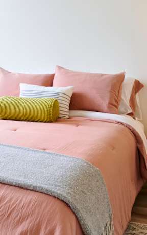 A bedroom with a pink bedspread and a grey blanket.