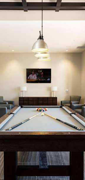A pool table is in the middle of a room with a TV and chairs.
