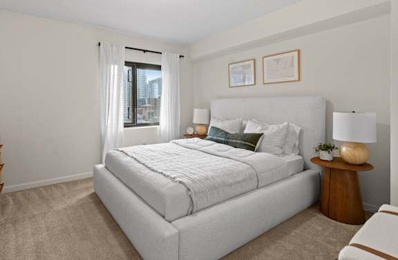 A bedroom with cream walls and tan carpet, and a bed with a white bedspread