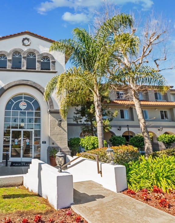 the front facade of a villa with palm trees and a flag