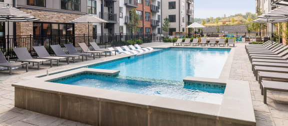 a swimming pool with chairs and umbrellas in front of an apartment building