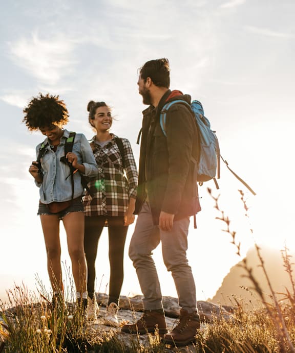 Three people are standing on a rocky hill with the sun setting in the background at Rosemeade Apartments, Roseville, 95661