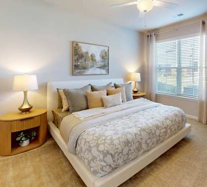 A bedroom with a large bed, a ceiling fan, and a painting on the wall.