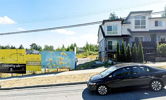 A black car is parked on the side of a road in front of a house.