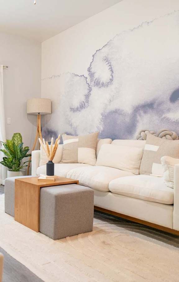 A living room with a white couch, a wooden side table, and a large painting on the wall.