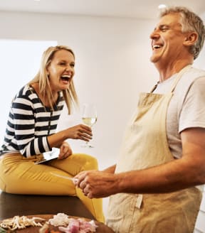 an older couple laughing and drinking wine in the kitchen