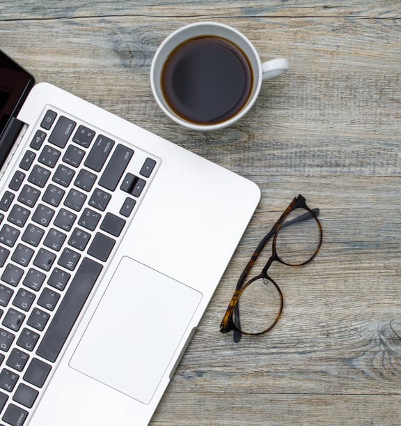 A laptop on a table with glasses and a cup of coffee