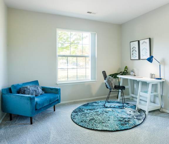 A blue couch sits in a room with a white desk and a rug.