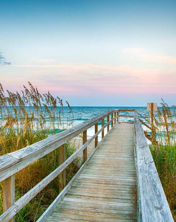 A wooden boardwalk leads to a beach with grasses on either side.
