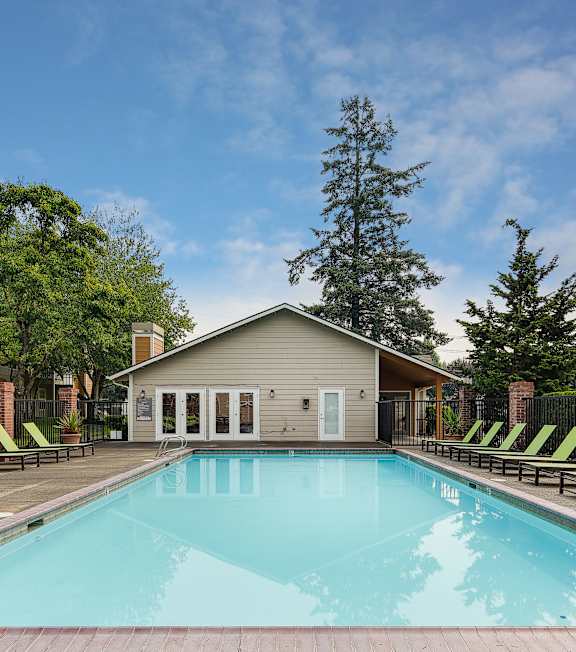 A swimming pool with lounge chairs and a house in the background.