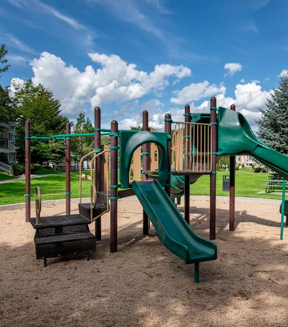 A playground with a green slide and a brown sandbox.