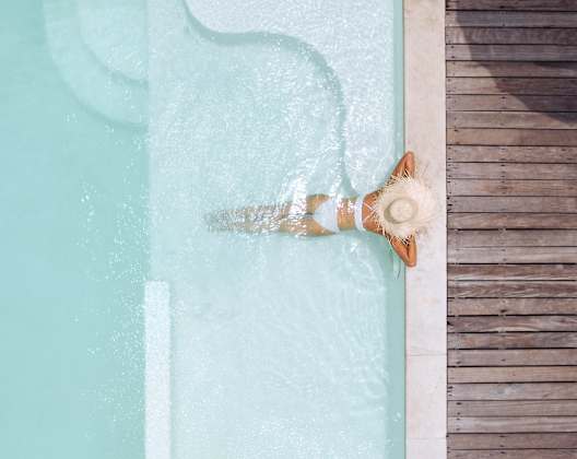 A person is sitting by a pool with a wooden deck.