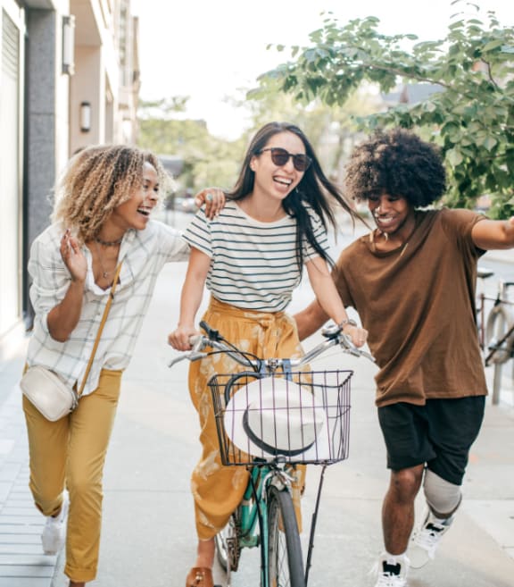 three young women walking a bike down a sidewalk