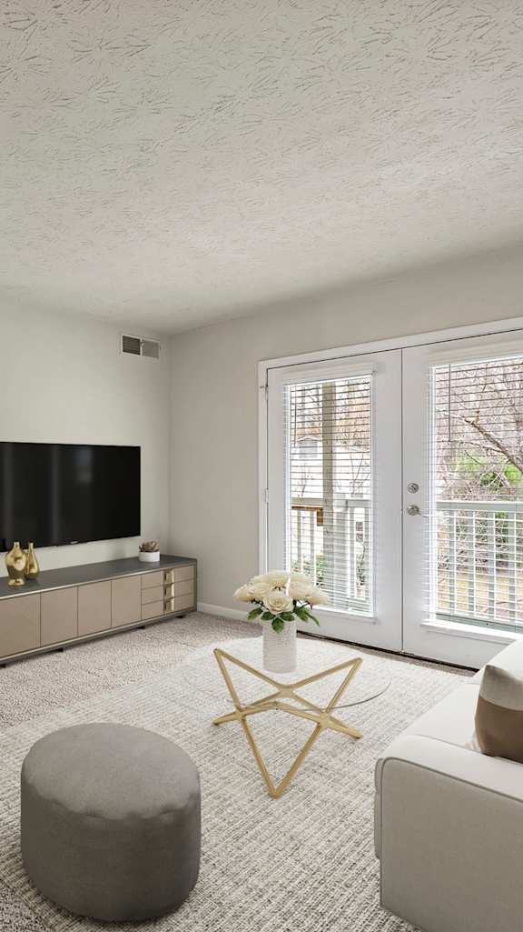 A living room with a grey ottoman, a white sofa, and a television.