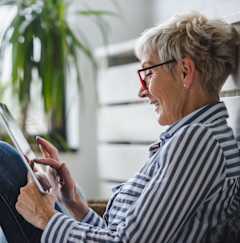 A woman with glasses is using a tablet while sitting on a bench.
