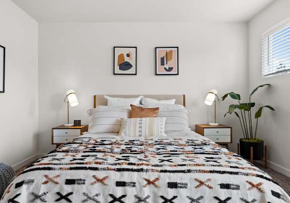 A bedroom with a bed covered in a quilt with an X pattern, two nightstands with lamps, and two framed pictures on the wall.