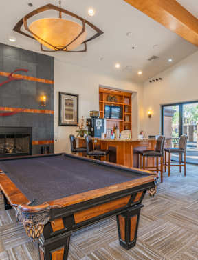 A pool table is in the middle of a room with a fireplace and a bar.