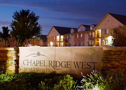 A sign for Chapel Ridge West Apartments is lit up at night.