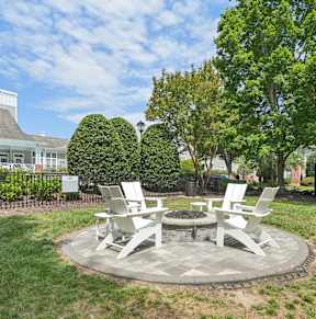 A round picnic table with four chairs around it is in the middle of a grassy area.