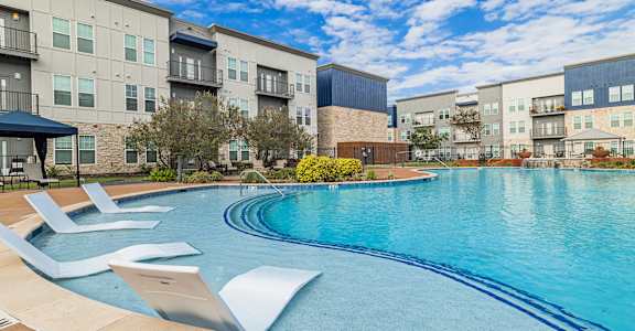 a swimming pool with lounge chairs in front of an apartment building