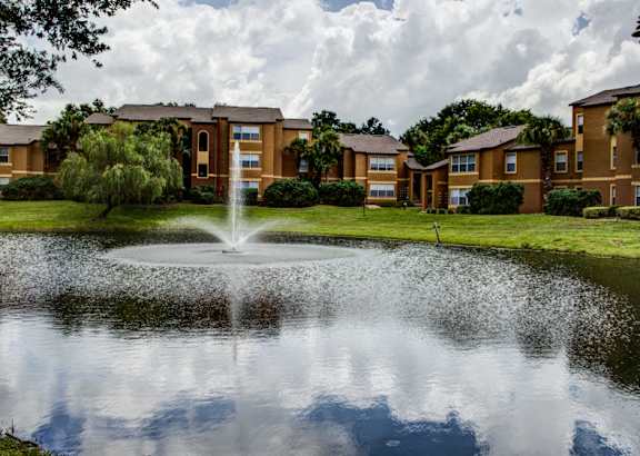 A fountain in the middle of a pond in front of apartment buildings.