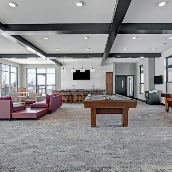 A wonderful resident lounge with tables, chairs, TVs, red couches, a kitchenette with a long bar with barstools, and a pool table at the Lafayette Apartment Homes. 