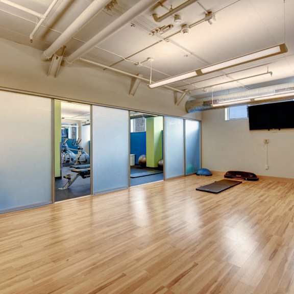 A large yoga room with hardwood floors and a flat screen tv on the wall at Avenir Apartments.