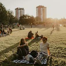 A group of people are sitting on a blanket in a park.