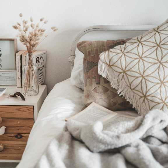 A bed with a white pillow and a grey blanket.