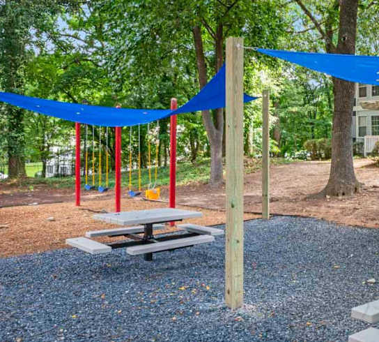 A playground with a blue canopy and a swing set.