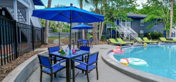 Blue patio tables and chairs with blue umbrellas next to community pool in Mandarin Bay apartments in Jacksonville, Florida.