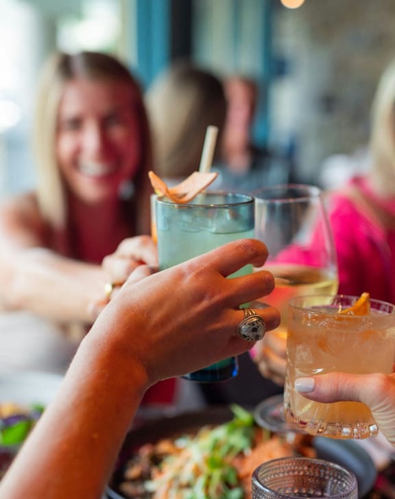 three women sitting at a table holding up cocktails at a restaurant