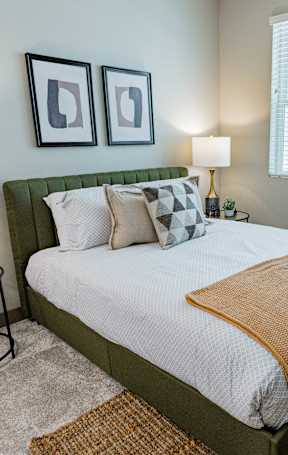 A bedroom with a bed, two lamps, a wardrobe, and two framed pictures on the wall.