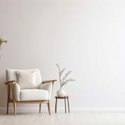 A white chair with a pillow sits next to a small plant in a pot.