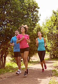 Three people running on a path in a wooded area.