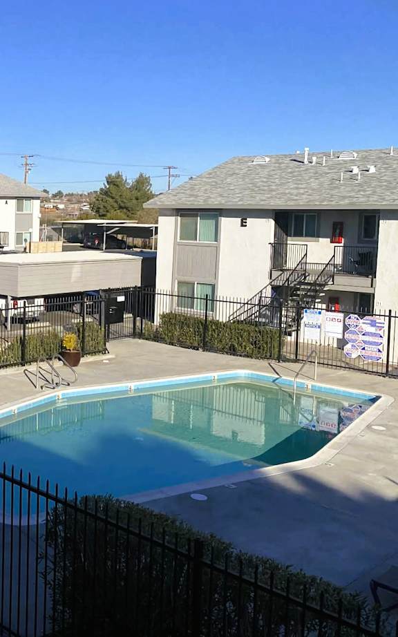 A pool surrounded by a black fence in front of apartment buildings.