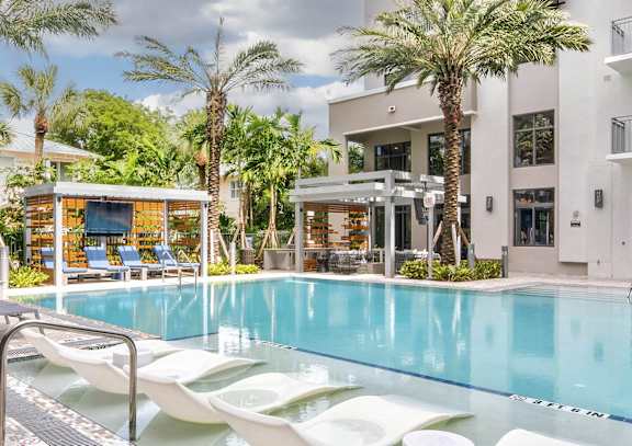 A pool with sun loungers and a building in the background.