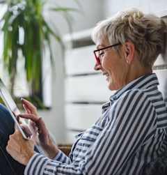 A woman with glasses is using a tablet while sitting on a bench.