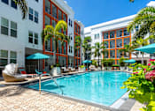 Thumbnail 30 of 40 - 3-Bedroom Apartments in Tampa, FL - Havana Square - Modern Resort-Style Swimming Pool with Umbrellas, Lounge Seats, Plants, and Palm Trees.