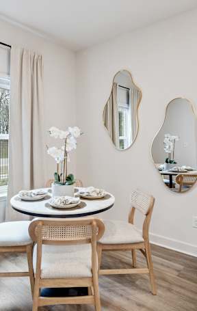 A dining room with a table set for two and a vase of white flowers.
